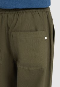 Olijfgroene broek met een comfortabele pasvorm, elastische tailleband en een grote achterzak. De stof lijkt zacht met een gladde textuur.