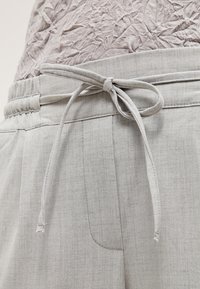 Ljusgrå, strukturerade byxor med elastisk midja och en knytning som detalj. Har sidofickor och subtila stygnaccentueringar.