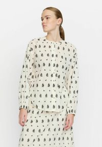 Camicia leggera a fantasia floreale in crema con disegni neri, maniche lunghe, orlo arrotondato e chiusura con bottoni. Tessuto morbido e semitrasparente.