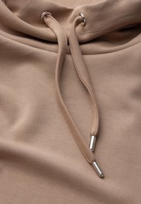 Felpa con cappuccio in tessuto beige con una superficie liscia. Caratterizzata da lacci con punte e occhielli metallici. Design semplice e minimale.