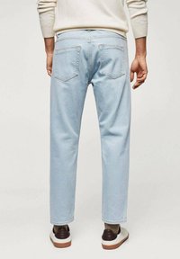 Jeans de mezclilla azul claro con corte recto, dos bolsillos traseros y detalles de costura mínimos, combinados con zapatillas oscuras marrones y blancas.