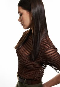 Top marrón texturizado con patrones ondulados horizontales, que presenta mangas cortas y una silueta ajustada, combinado con un cinturón y pantalones de color verde oliva.