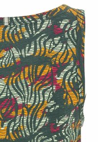 Tissu à motifs avec des lignes ondulées en vert, rouge, jaune et blanc. Texture douce avec un col rond et des détails de couture visibles.