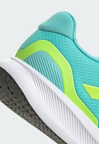 Turquoise athletic shoe with a textured mesh upper, a lime green accent, and a white, ridged sole. Features prominent traction pattern on the outsole.