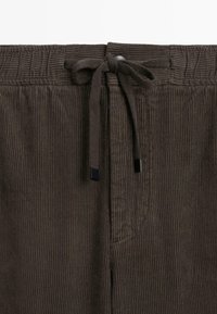 Brune corduroy bukser med en elastisk talje og snøre, samt forlommer. Stoffet har en ribbet tekstur og en glat overflade.