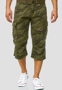 Kamuflasje cargo shorts i olivengrønn stoff, med flere lommefester, oppbrettede sømmer og beltestropper, kombinert med hvite joggesko.