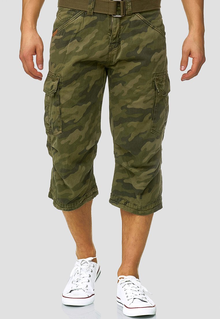 Kamuflasje cargo shorts i olivengrønn stoff, med flere lommefester, oppbrettede sømmer og beltestropper, kombinert med hvite joggesko.