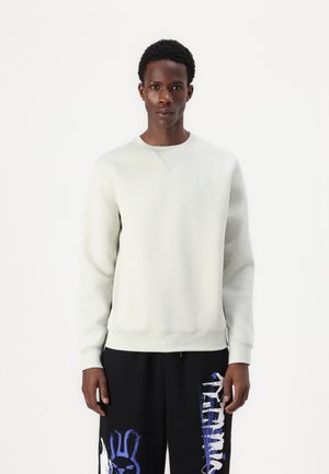 Light grey sweatshirt with a crew neckline and ribbed cuffs, made from soft fabric. Worn over black pants featuring colorful graphic designs.
