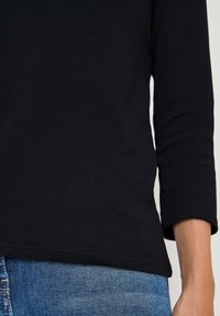 Schwarzes Langarmshirt aus weicher Baumwolle mit rundem Halsausschnitt und geradem Saum, kombiniert mit blauen Denim-Jeans.