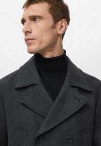 Abrigo gris de espina de pescado con cierre cruzado, solapas con muesca y un suéter de cuello alto negro debajo. Textura lisa, ajuste estructurado.