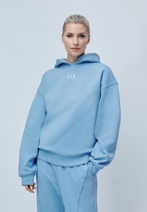 Lyseblå hettegenser laget av mykt stoff, med kengurulomme, ribbestrikkede ermer og et brodert logo på brystet.