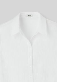Chemise blanche à boutons texturée avec un col évasé. Présente un motif subtil et des boutons transparents le long de la patte de boutonnage.