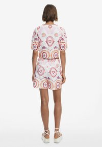 Tvådelad outfit bestående av en kort topp och shorts i ett vitt tyg prytt med färgglada blommönster i orange, rosa och lila.