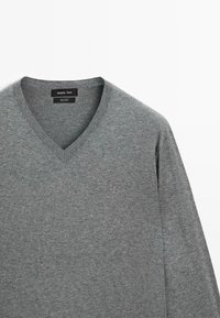 Grau V-Ausschnitt-Pullover aus Baumwolle, mit einer weichen Textur und langen Ärmeln. Etikett sichtbar, das Marke und Stoffzusammensetzung angibt.