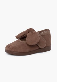 Chaussure en daim marron avec un bout arrondi, présentant un grand nœud à l'avant et une semelle en caoutchouc basse. Texture douce et design à enfiler.