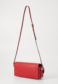 Röd lädercrossbody-väska med rektangulär form, justerbar rem och guldfärgad hårdvara. Slät textur och minimalistisk design.