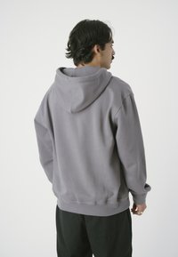 Pullover hoodie in grey, made from soft fabric with a relaxed fit. Features a hood, dropped shoulders, and ribbed cuffs. Smooth texture.