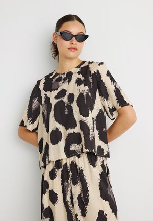 Beiges kurz geschnittenes Top mit großem schwarzem und grauem Tierprint. Kurze Ärmel, rundhalsausschnitt, kombiniert mit passendem gemustertem Unterteil.