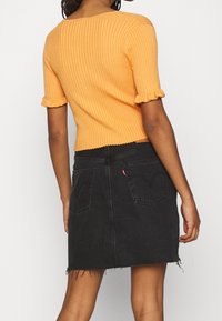 Pomarańczowy prążkowany top z krótkim rękawem i falbankami na mankietach, zestawiony z czarną spódnicą dżinsową z postrzępionymi brzegami i kieszeniami z tyłu.