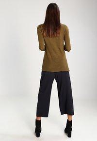 Top a costine di colore verde oliva, con un retro leggermente più lungo, abbinato a pantaloni navy a gamba larga e stivaletti neri con tacco.