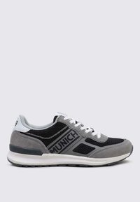 Zapatilla deportiva gris y negra con paneles de malla, detalles de ante, cordones blancos y un logo que dice "MUNICH" en el lateral. Suela de goma con agarre.