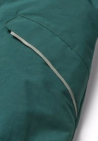 Grön tyg med en slät textur har en kontrasterande grå accent längs kanten och en ficka med en klaffdetalj.