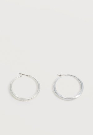 Pendientes de aro de metal plateado con superficie lisa y ligeramente curvada y cierre de tipo mosquetón sobre un fondo blanco liso.