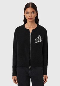 Cardigan nero con zip e collo rotondo, realizzato in tessuto morbido. Presenta una superficie testurizzata e un design grafico bianco sul petto.