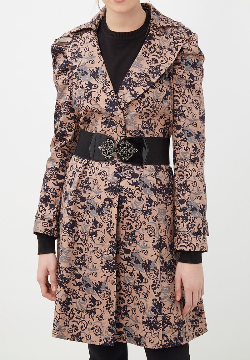 Trench de color rosa claro con un estampado floral, cuello estructurado, cinturón negro con hebilla ornamentada y detalles en puños de punto negros.