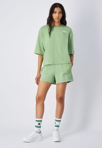 Camiseta de algodón verde claro con mangas cortas y un gráfico circular. Combinada con pantalones cortos a juego y zapatillas blancas, acentuada por calcetines a rayas.