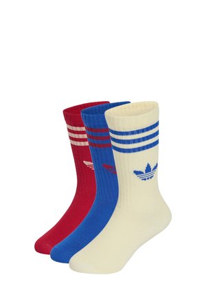 Kolme paria Adidasin nilkkasukkia punaisena, sinisenä ja valkoisena, jokaisessa kolme raitaa ja Adidasin kolmilehtinen logo lähellä kärkeä.