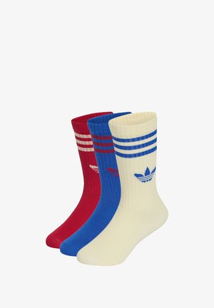 Trzy pary skarpetek Adidas za kostkę w kolorach czerwonym, niebieskim i białym, każda z trzema paskami i logo trefoil Adidas u góry.