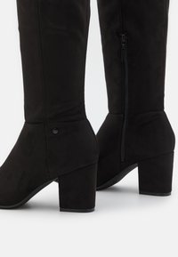 Botas negras hasta la rodilla de ante, con tacón cuadrado, cremallera lateral y detalles de costura mínimos para una apariencia elegante.