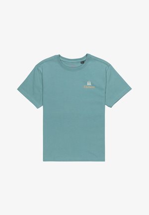 Camiseta de algodón de color azul claro con mangas cortas y cuello redondo, que presenta un pequeño logo naranja. Se lleva con pantalones de mezclilla azul claro y zapatos oscuros.