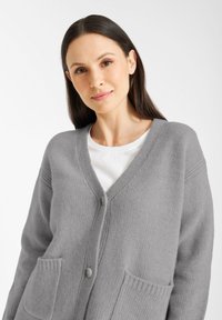 Lichtgrijze cardigan van gestructureerd breimateriaal, met een v-hals, knoopsluiting aan de voorkant en twee voorzakken.