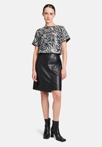 Schwarzes, kurzärmliges Top mit Pailletten und wellenförmigem Muster, kombiniert mit einem hoch taillierten schwarzen Lederrock und schwarzen, hohen Ankle Boots.