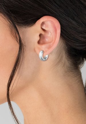 Orecchini a cerchio in argento con una fascia texturizzata, caratterizzati da un design circolare elegante e una finitura lucida, indossati su un lobo dell'orecchio.