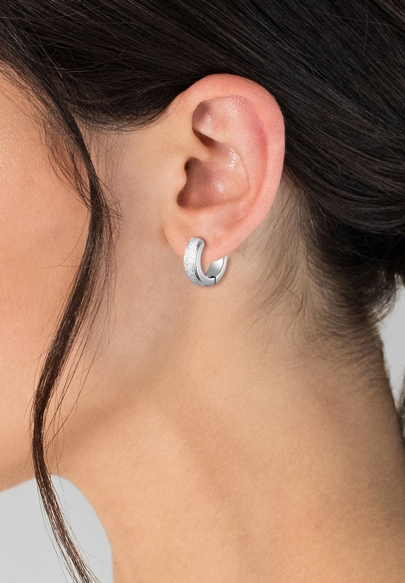 Orecchini a cerchio in argento con una fascia texturizzata, caratterizzati da un design circolare elegante e una finitura lucida, indossati su un lobo dell'orecchio.