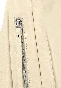 Material din piele de culoare crem, cu o suprafață texturată, având o închidere cu fermoar argintie și detalii de cusătură contrastante.