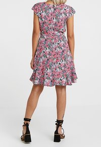 Abito floreale con maniche a volant, caratterizzato da un motivo rosa e nero, vita stretta e gonna a ruota; indossato con tacchi alti e cinturini alla caviglia.