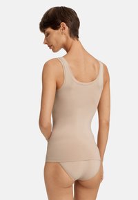 Krémová tílko s širokými ramínky, bezešvou konstrukcí a hladkým povrchem, v kombinaci s odpovídajícími spodními kalhotkami, z pohledu zezadu.
