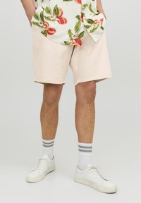 Shorts rose clair à coupe décontractée, fabriqués en tissu doux. Associés à des baskets blanches et des chaussettes rayées blanches et grises.