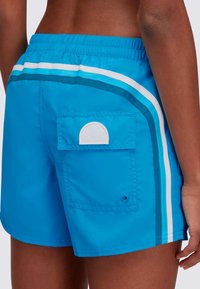 Blauwe zwemshorts hebben een twee-kleurig ontwerp met witte en teal strepen, een elastische tailleband en een achterzak met een witte accent.
