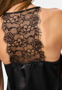 Crna satenska košuljica s cvjetnom čipkastom leđima s valovitim rubovima i glatkom, sjajnom teksturom. Tanji naramenici upotpunjuju dizajn.