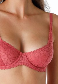 Reggiseno in pizzo color rosa polveroso, con ferretti, spalline regolabili e motivo floreale. Tessuto liscio con bordi ondulati lungo le coppe.
