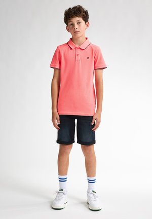 Roze katoenen polo met een kraag, zwarte afwerking en klein logo. Draagt met donkere spijker shorts en witte sneakers. Blauw gestreepte sokken.