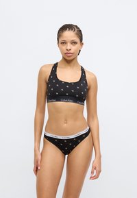 Μαύρο αθλητικό σουτιέν και μαύρο κάτω μέρος μπικίνι με επαναλαμβανόμενο μοτίβο λευκού λογότυπου. Μαλακό ύφασμα με λεπτομέρειες ελαστικής μέσης.