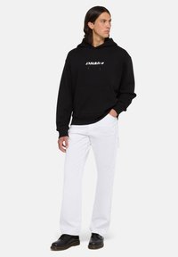 Sudadera con capucha negra y logo blanco, combinada con pantalones blancos holgados y zapatos negros. Cuenta con un bolsillo tipo canguro y capucha con cordón.