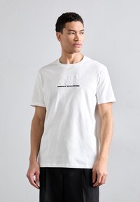 Valge puuvilla t-särk, millel on tekstuuriga logo "AX" ja "Armani Exchange" mustal taustal, lühikesed varrukad ja vabalt langev sobivus.