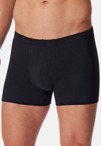 Boxers en coton noir avec une taille sans couture et une coupe ajustée. Le tissu est doux et lisse, avec un design simple et uni.
